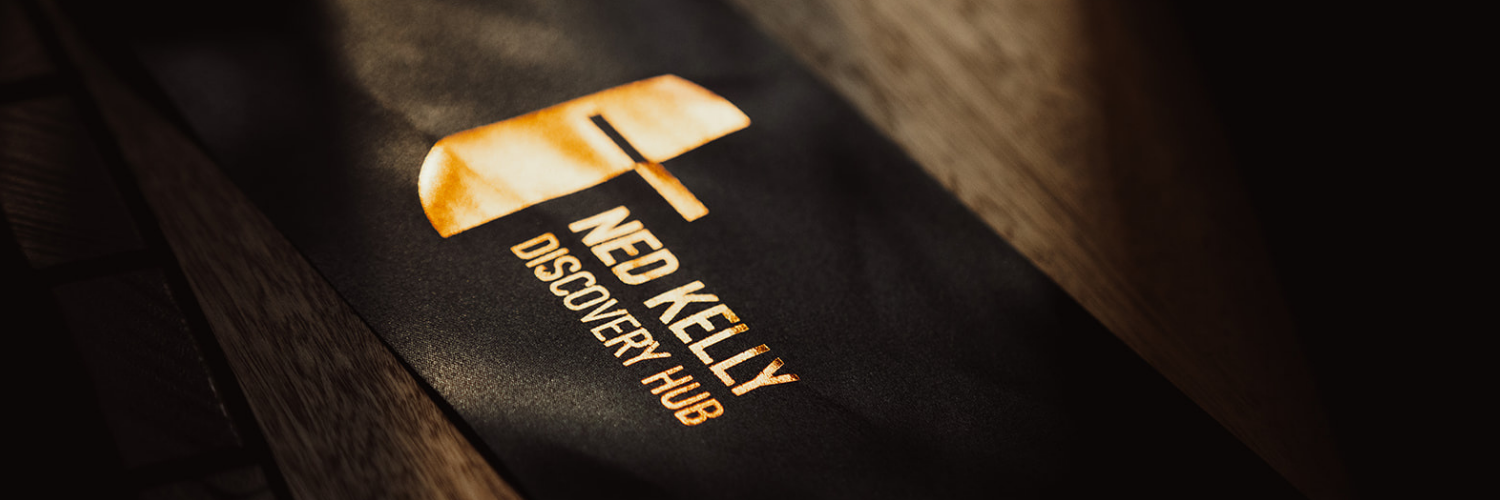 Close-up of the Ned Kelly Discovery Hub logo featuring a stylized helmet design on a dark background.