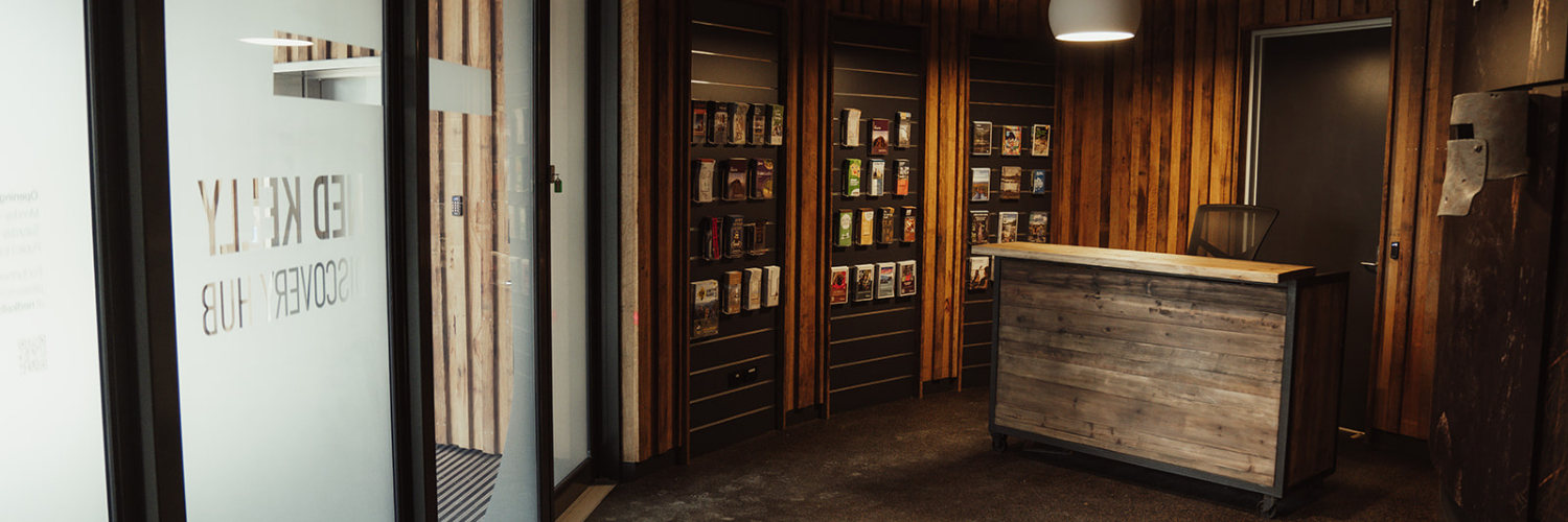 Interior view of the Ned Kelly Discovery Hub visitor information area with a rustic timber counter and brochure display shelves.